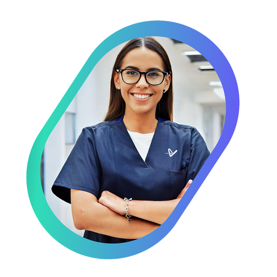 Smiling female healthcare professional in navy scrubs with arms crossed, standing in a bright hospital corridor.